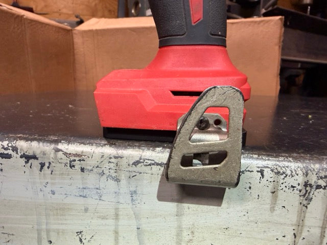 Milwaukee M18 drill on a Keepfast tool holder at the edge of a workbench, belt clip hanging past the edge